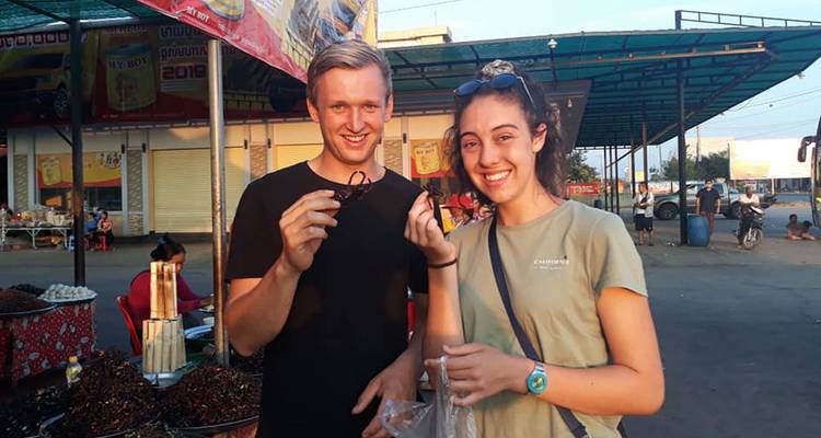 Twee mensen die eten vasthouden op een markt onder een gedeeltelijk overdekte ruimte.