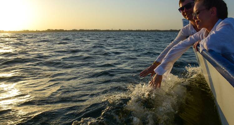 Deux personnes sur un bateau profitant de l'eau avec le coucher de soleil en arrière-plan.