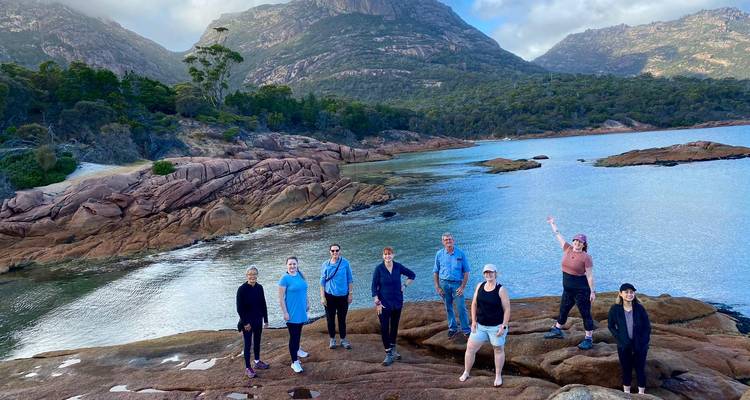 Groep mensen op rotsen bij het water met bergen.
