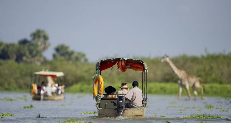 Des touristes dans des bateaux regardent une girafe.