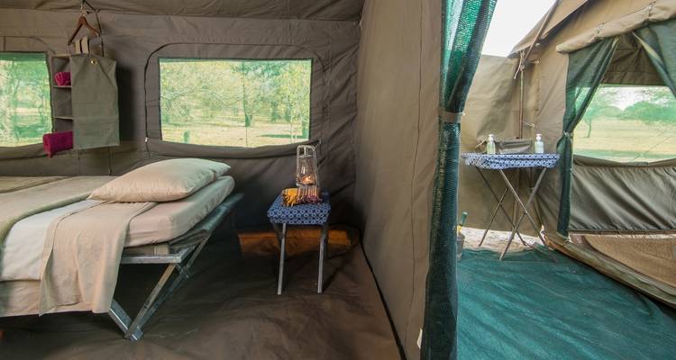 Intérieur d'une tente de safari avec un lit, une lanterne et vue sur l'extérieur.