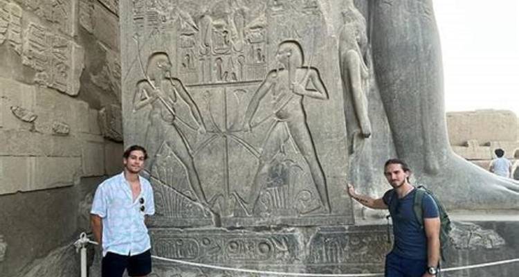 Zwei Touristen stehen neben einem antiken geschnitzten Monument.