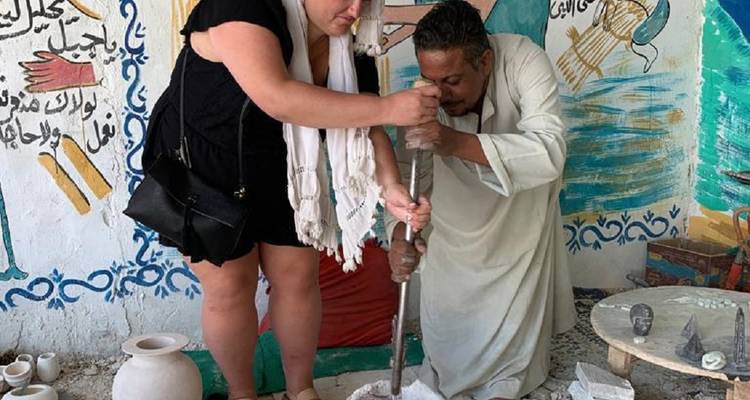 Un turista ayuda a un artesano local moliendo polvo de piedra dentro de un colorido taller.
