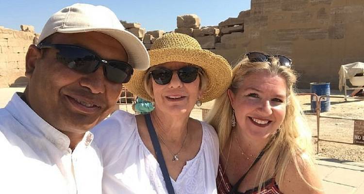 Selfie alegre en primer plano de tres viajeros en un sitio arqueológico soleado con bloques de piedra detrás.