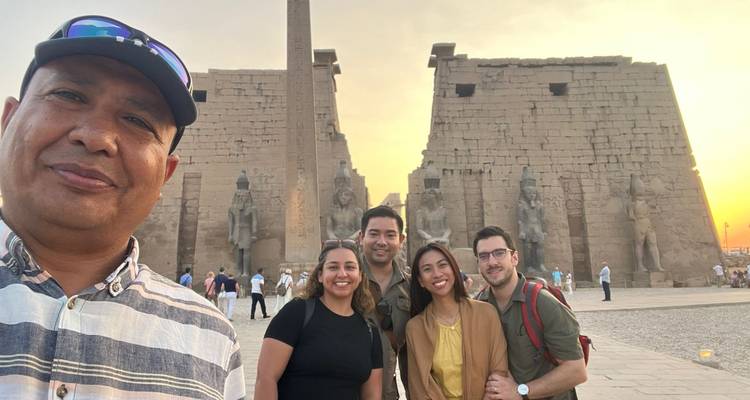 Een groep glimlacht bij zonsondergang met de verlichte pyloon van de Luxor Tempel op de achtergrond, gids op de voorgrond.