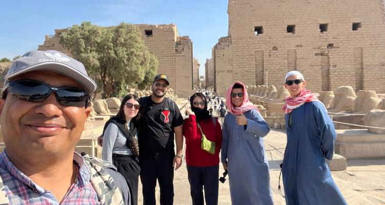 Gids en reizigers glimlachen voor selfie bij de ruïnes en ramskop-sfinxen van de Karnak Tempel.