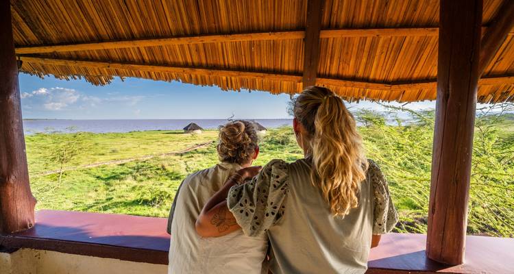 Pareja disfrutando de una vista desde una cabaña con techo de paja junto a un lago.