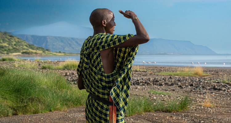 Una persona con vestimenta tradicional mirando hacia un lago con montañas distantes.