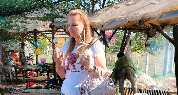 Een toerist proeft lokale snacks bij een kraampje op een openluchtmarkt in Cambodja dat wordt beschaduwd door zeilen en bomen.