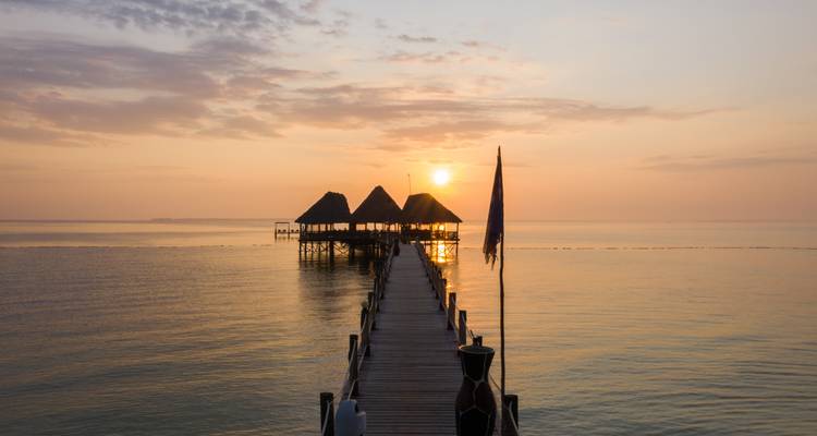 Zonsondergang boven de oceaan met een pier en hutten.