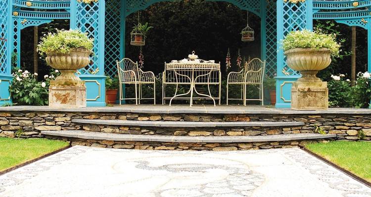 Elegante turquoise prieel omgeven door verzorgde tuin, stenen trappen en een mozaïek pauwmotief.