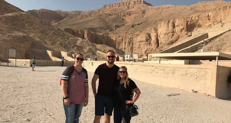 Drei Touristen posieren mit Wüstenhügeln im Hintergrund.