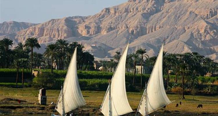 Bateaux à voile traditionnels sur le Nil avec des montagnes désertiques en arrière-plan.