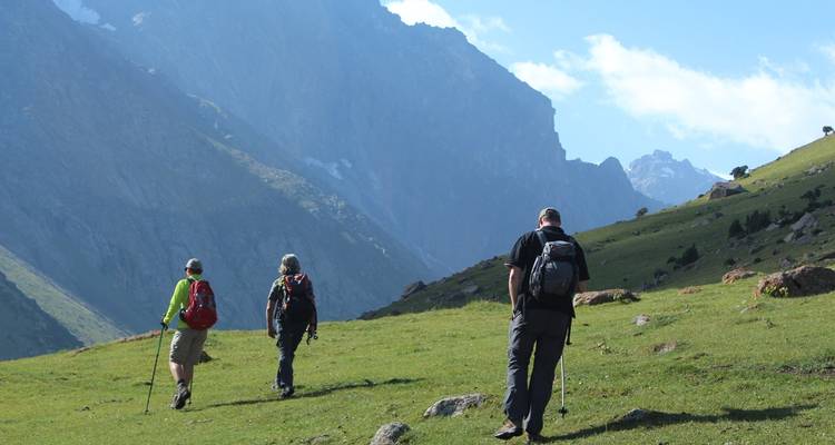 Trois randonneurs traversant un paysage vallonné avec un arrière-plan montagneux.