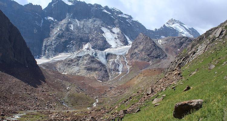 Vallée rocheuse avec des pentes parsemées de neige et un glacier au loin.