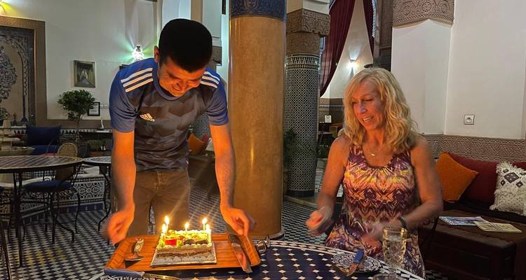 Un hombre presenta un pastel de cumpleaños encendido a una mujer sonriente en un restaurante riad de azulejos con ambiente.