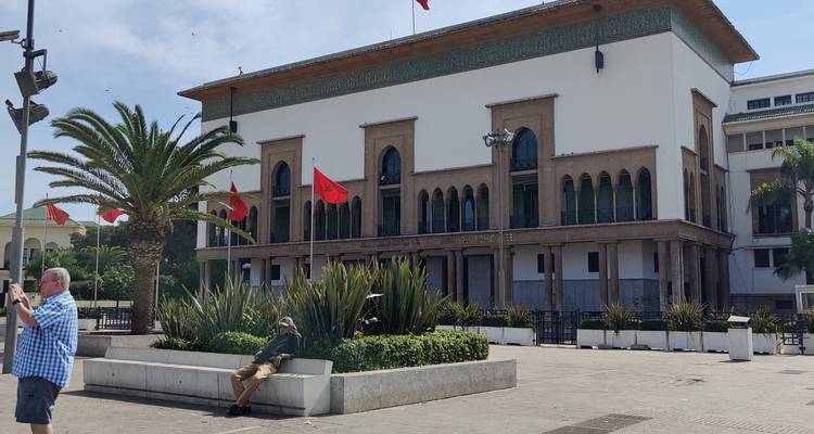 Amplia plaza con palmeras, banderas marroquíes y el Ayuntamiento de Casablanca de estilo art déco, visitantes tomando fotos.