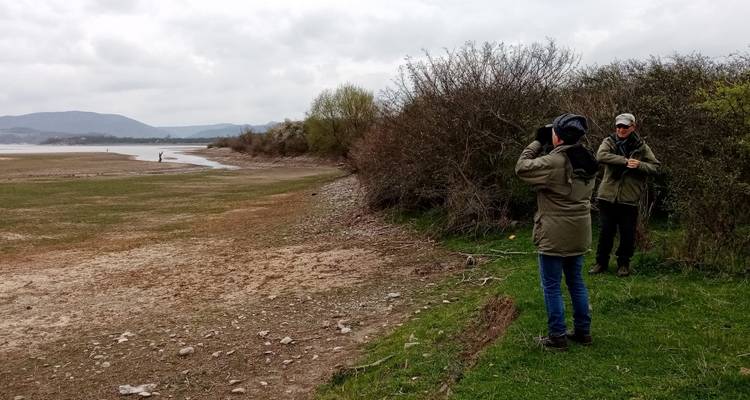 Des gens avec des jumelles au bord d'un lac contemplant des collines lointaines.