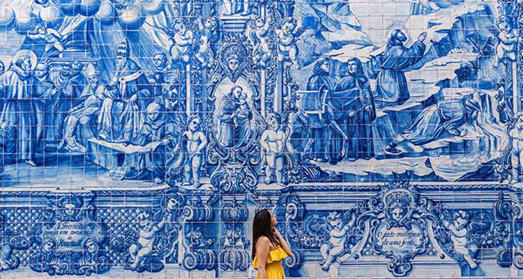 Frau in einem gelben Kleid bewundert ein kunstvolles blau-weißes Azulejo-Fliesenwandgemälde.