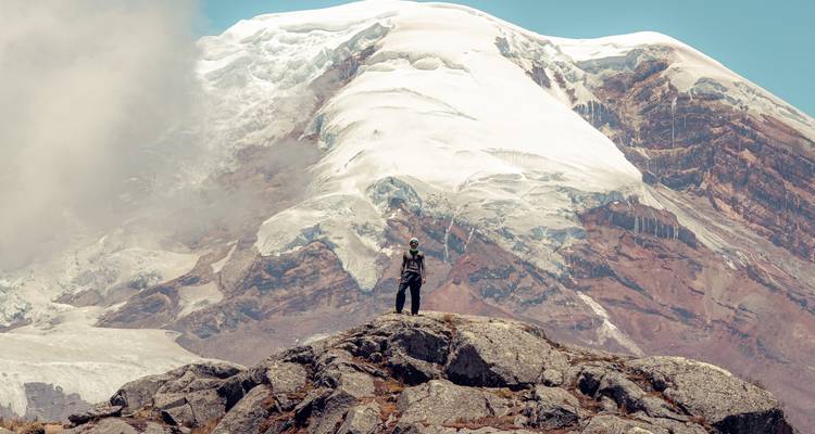 Un aventurier solitaire se tient sur un escarpement rocheux face au sommet massif aux pics de glace de Chimborazo.