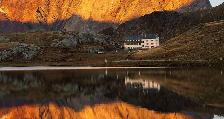 Une maison au bord d'un lac avec des montagnes illuminées par le coucher de soleil.