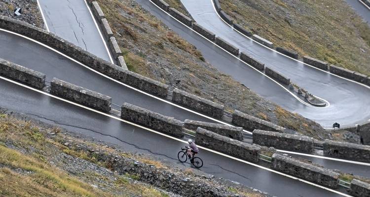 Cycliste sur une route de montagne sinueuse avec des barrières rocheuses.