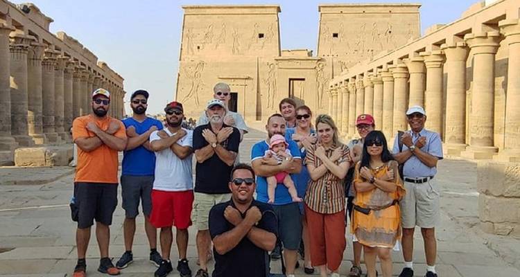 Große Reisegruppe posiert vor den Säulen und Pylonen des Philae-Tempels und macht Armzeichen.