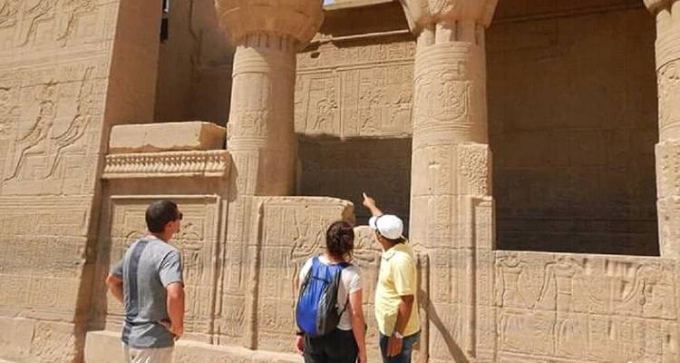 Führer zeigt auf detaillierte Schnitzereien an Sandsteinsäulen, während zwei Touristen aufmerksam zuhören.