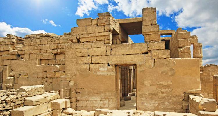Ruinas con intrincados tallados en piedra bajo un cielo parcialmente nublado.