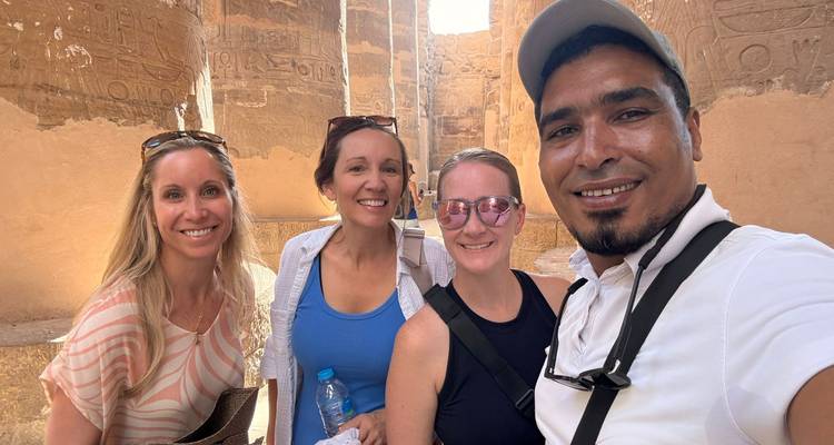 Gids en drie vrouwen glimlachend in de beschaduwde zandstenen hal van de Karnak Tempel.