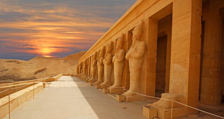Primer plano de estatuas en el Templo Mortuorio de Hatshepsut con una puesta de sol dramática.