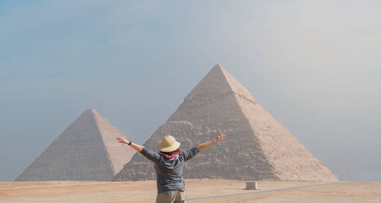 Une personne avec les bras étendus devant les pyramides.