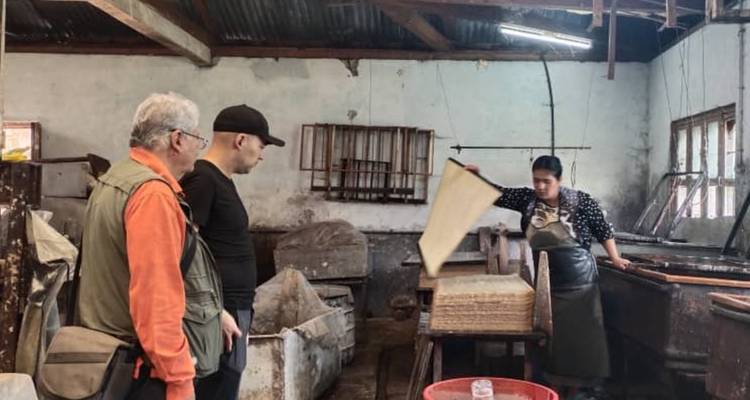 Trois personnes observant un processus de fabrication de papier à l'intérieur d'un atelier.