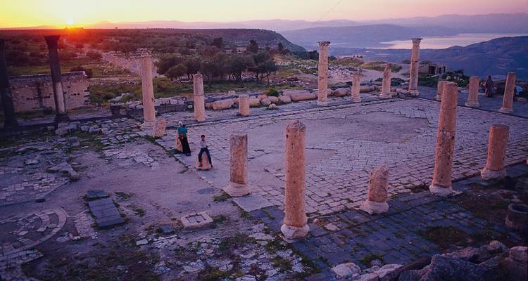 Sunset over ancient ruins with two people walking.