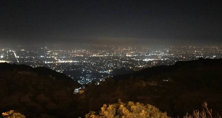 Vue nocturne d'une ville avec des lumières vives et des collines sombres.