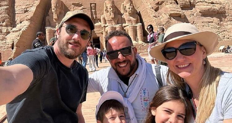 Glimlachende familie die een selfie maakt voor de gigantische zittende beelden van Abu Simbel onder de felle zon.