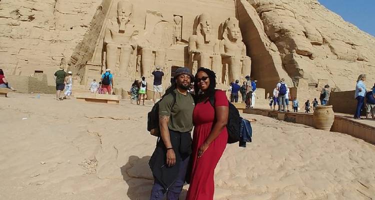 Stel dat arm in arm poseert op zandgrond met de monumentale standbeelden van Abu Simbel achter hen.