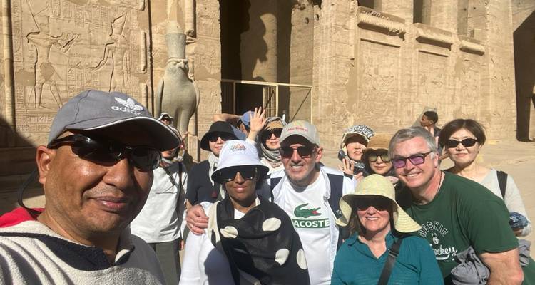 Toeristen die samen poseren in een zonnige binnenplaats van een Egyptische tempel met gebeeldhouwde stenen muren en een valkeisstandbeeld
