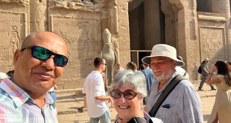 Kleine toergroep die glimlacht naast uitgehouwen tempelmuren en stenen valkeisbeeld in Egypte