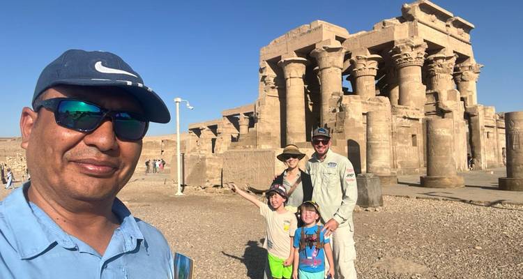 Gids en familie poseren met jonge kinderen voor de dubbelkolommade gevel van de Kom Ombo-tempel op een heldere dag