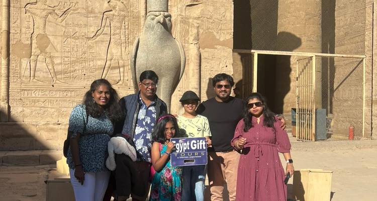 Familie met rondleiding bord poseren onder een valkebeeld op het voorplein van de Edfu-tempel
