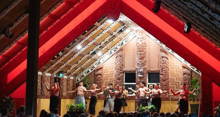 Des artistes maoris présentent un spectacle culturel à l'intérieur d'une maison de réunion sculptée baignée d'une lumière rouge.