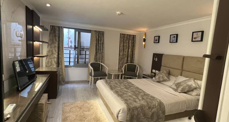 Bright, neutral-toned hotel room with a double bed, seating area and framed art on the walls.