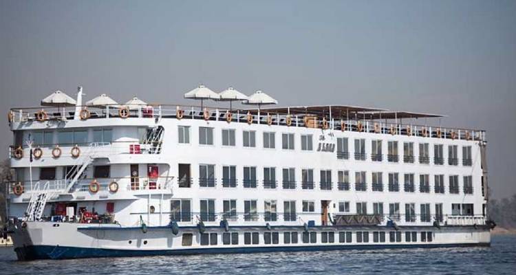 A multi-deck Nile cruise ship sails on calm water under a clear sky.