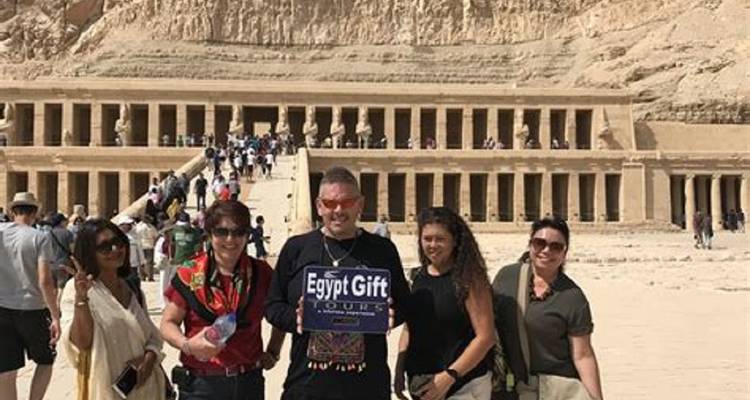 A small group poses with a tour sign in front of the Temple of Hatshepsut at Deir el-Bahri.