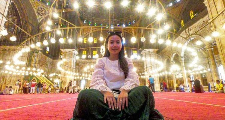 Femme assise à l'intérieur d'une mosquée avec des lustres illuminés.