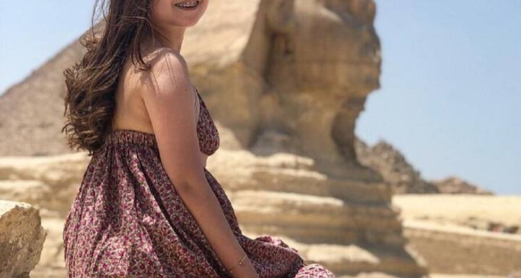 Jeune femme assise avec une pyramide et le Sphinx en arrière-plan.