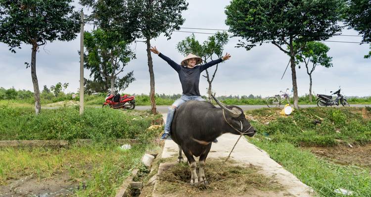 Eine Person, die fröhlich auf einem Wasserbüffel in einer ländlichen Umgebung reitet.