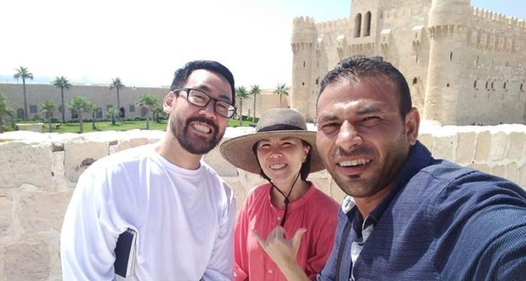 Trois personnes posant devant une forteresse historique par une journée ensoleillée.