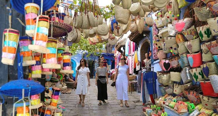 Tres personas caminando por una calle de mercado vibrante con cestas y textiles.